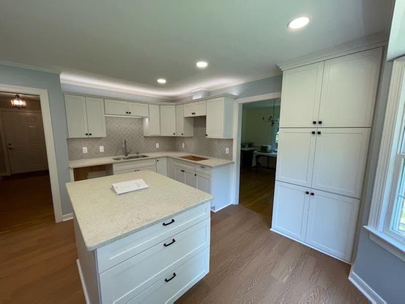 Modern kitchen with white cabinetry, quartz countertop island, and hardwood flooring.