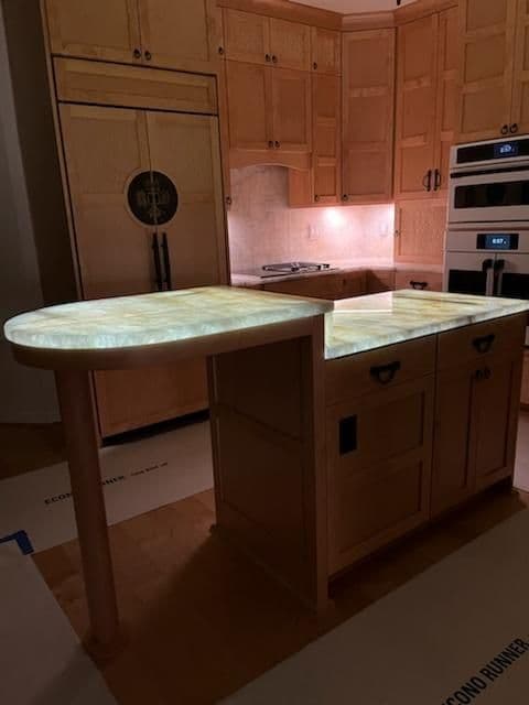 Illuminated onyx kitchen island with wooden cabinetry and modern appliances.