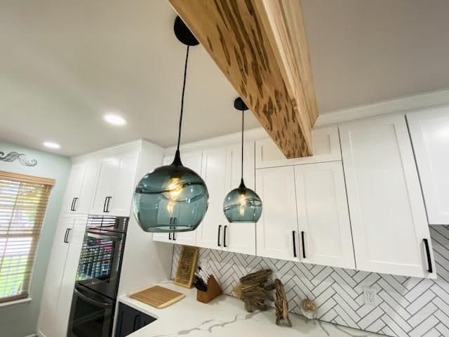 Modern kitchen featuring wood beam and stylish pendant lights over white cabinets.