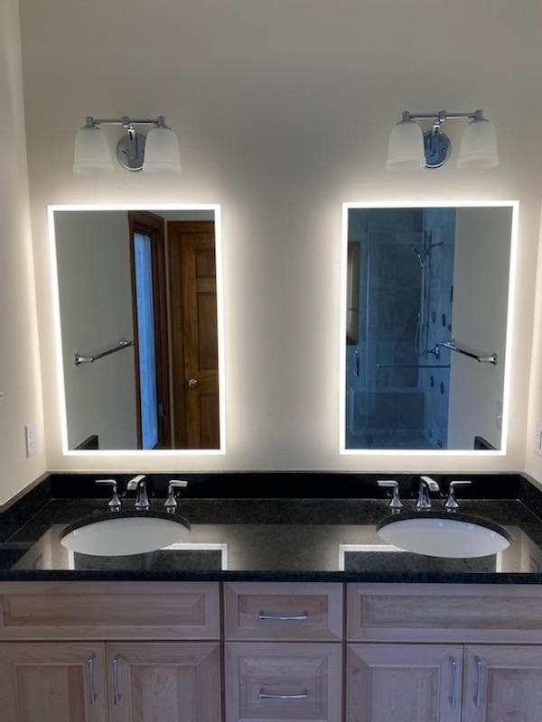 Modern bathroom with illuminated mirrors, dual sinks, and stylish fixtures.