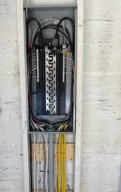 Electrical panel with circuit breakers and wiring inside a wooden wall.