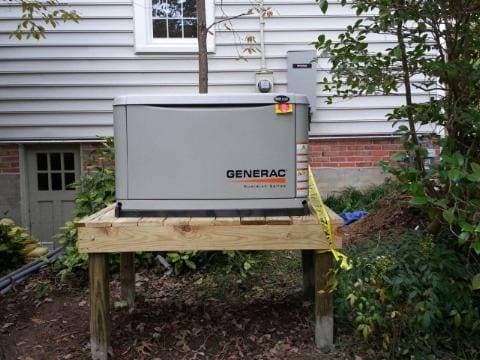 Generac generator installed on a wooden platform outside a house for reliable backup power.