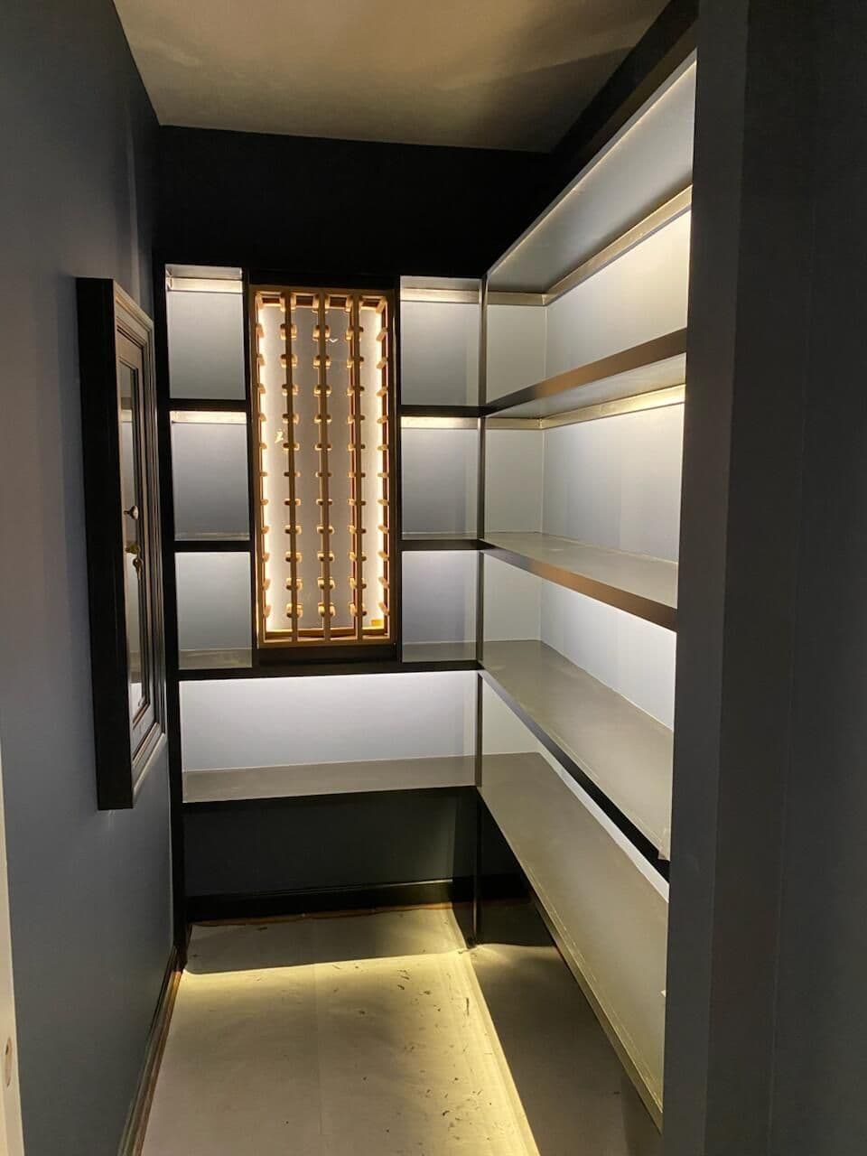 Interior of a modern pantry with illuminated shelves and dark walls, featuring a stylish window.