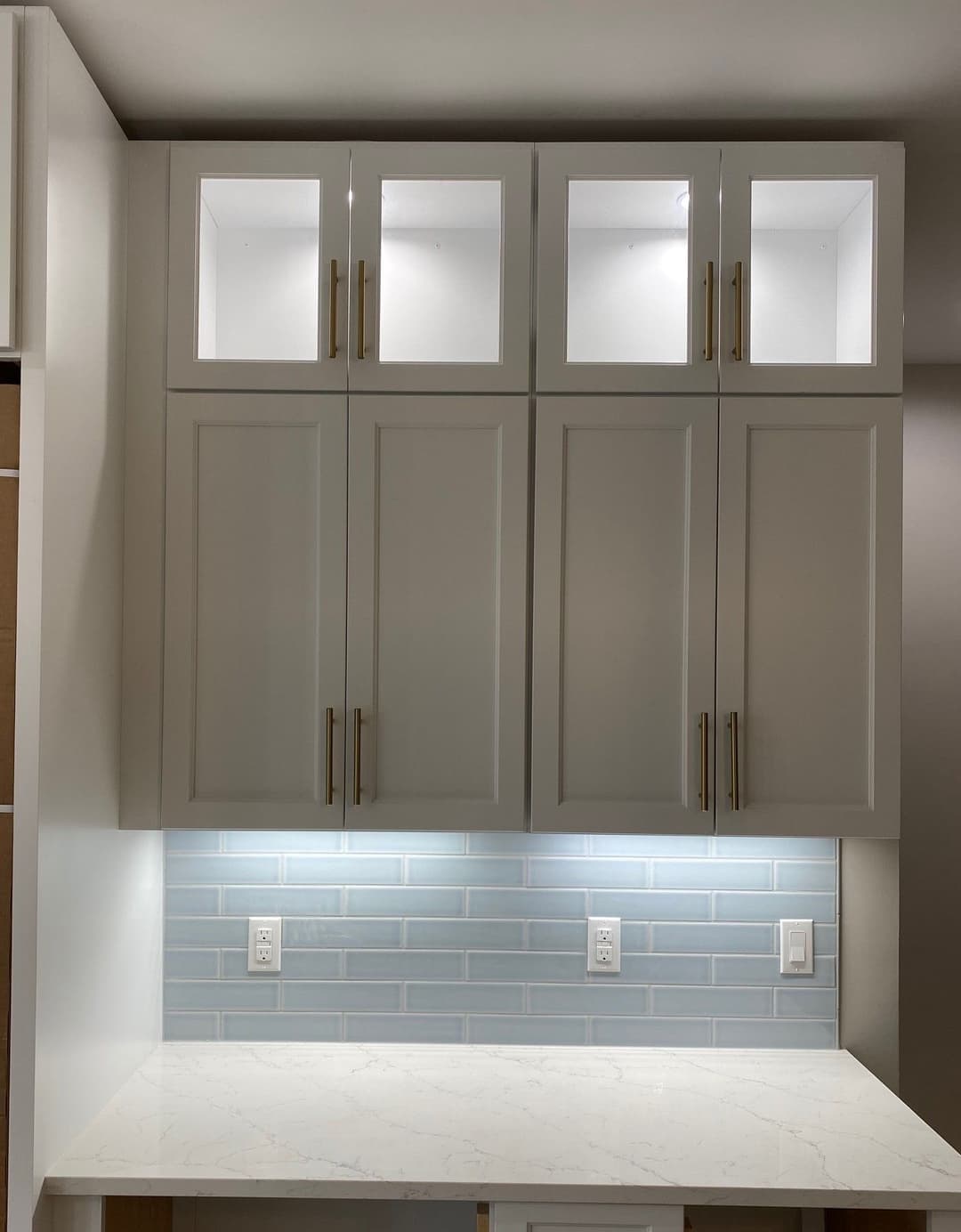 Modern kitchen cabinetry with glass-front doors and blue subway tile backsplash.