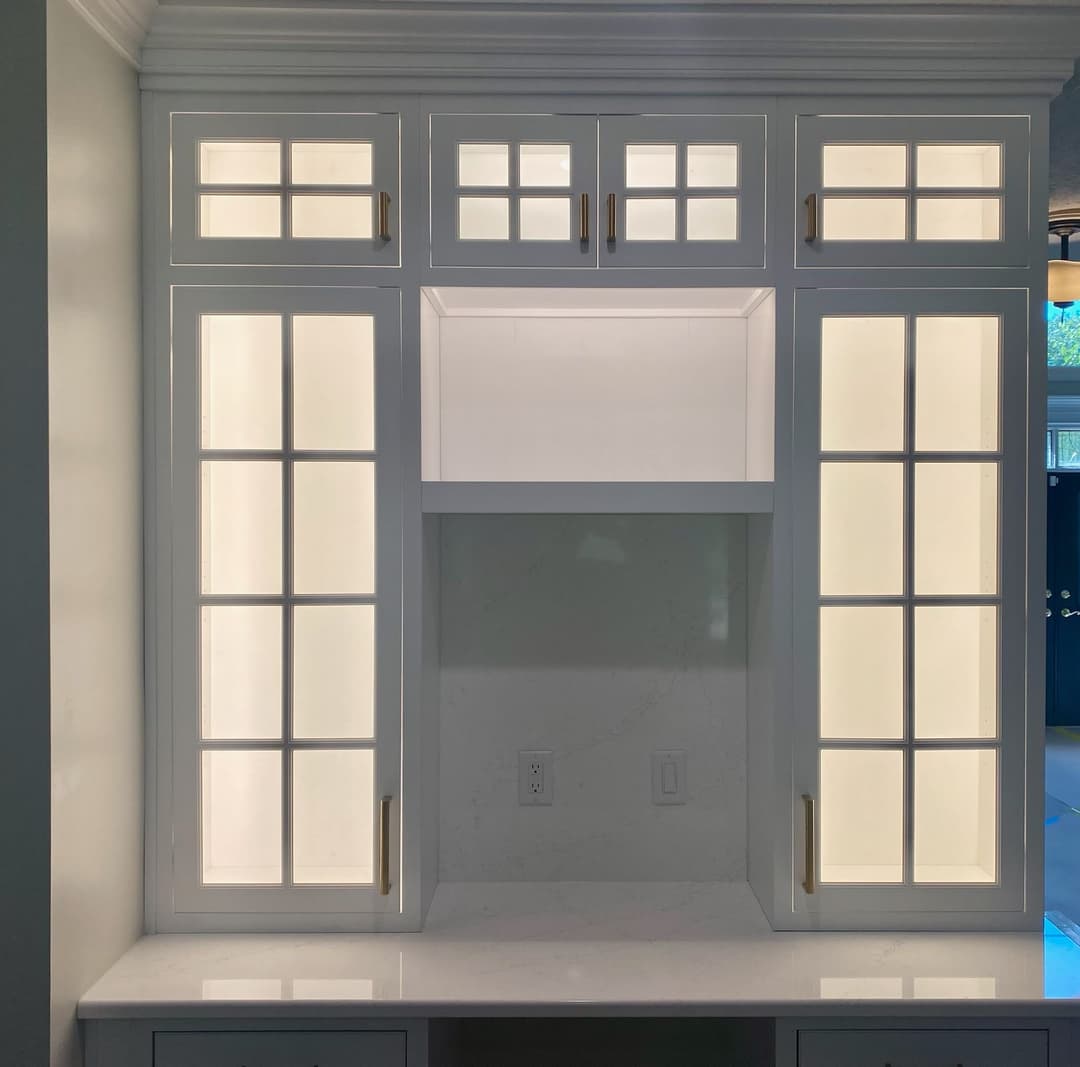 Modern white cabinetry with glass doors and backlighting for stylish home organization.