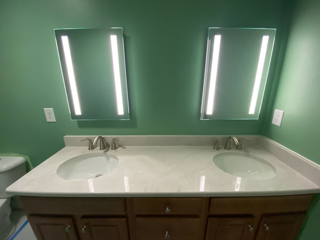 Modern bathroom with dual vanity, green walls, and illuminated mirrors.