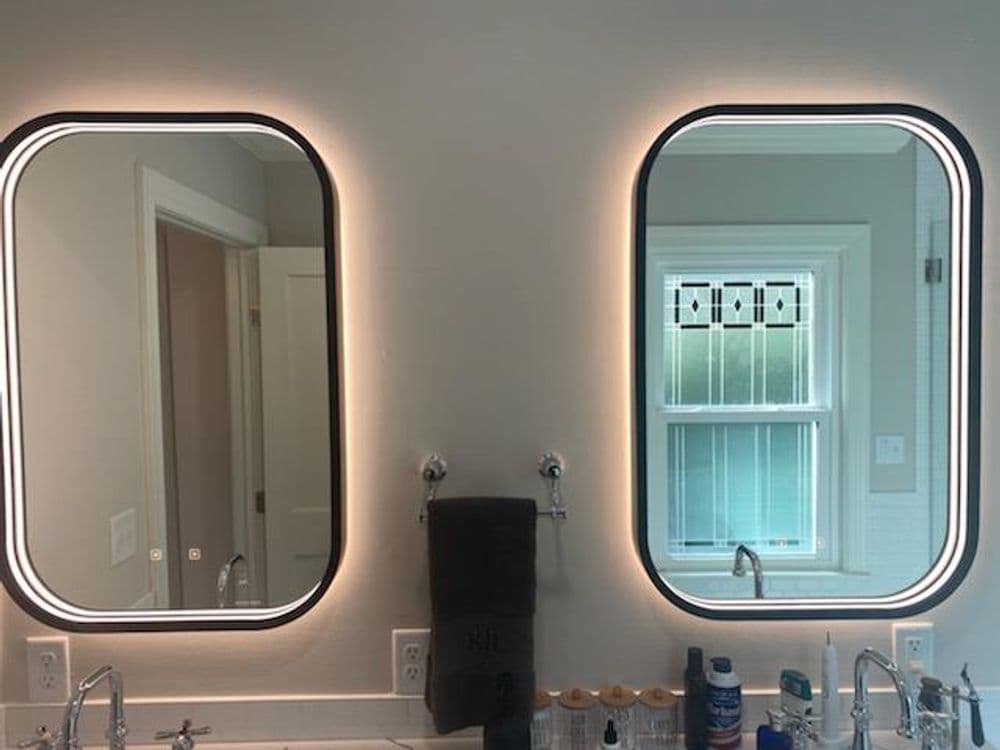 Modern illuminated bathroom mirrors with soft backlighting, reflecting a window view.
